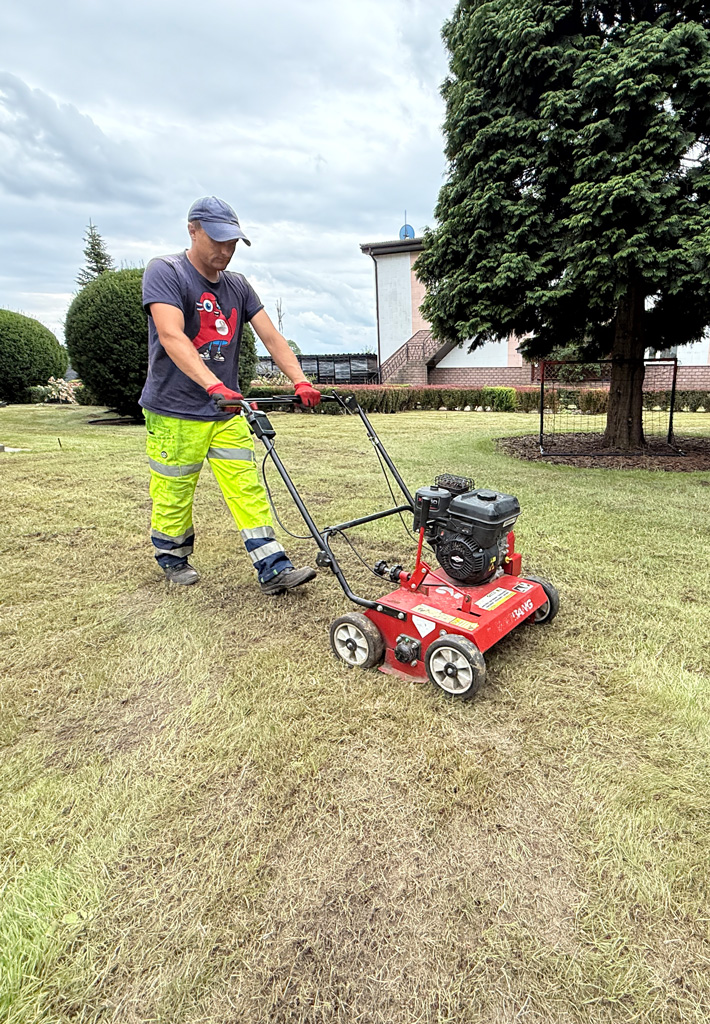 Mężczyzna wykonuje wertykulacje trawnika u klienta