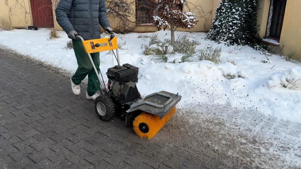 Zamiatanie i usuwanie śniegu z chodnika zamiatarką mechaniczną STIGA, zimowe utrzymanie nawierzchni przed budynkiem.