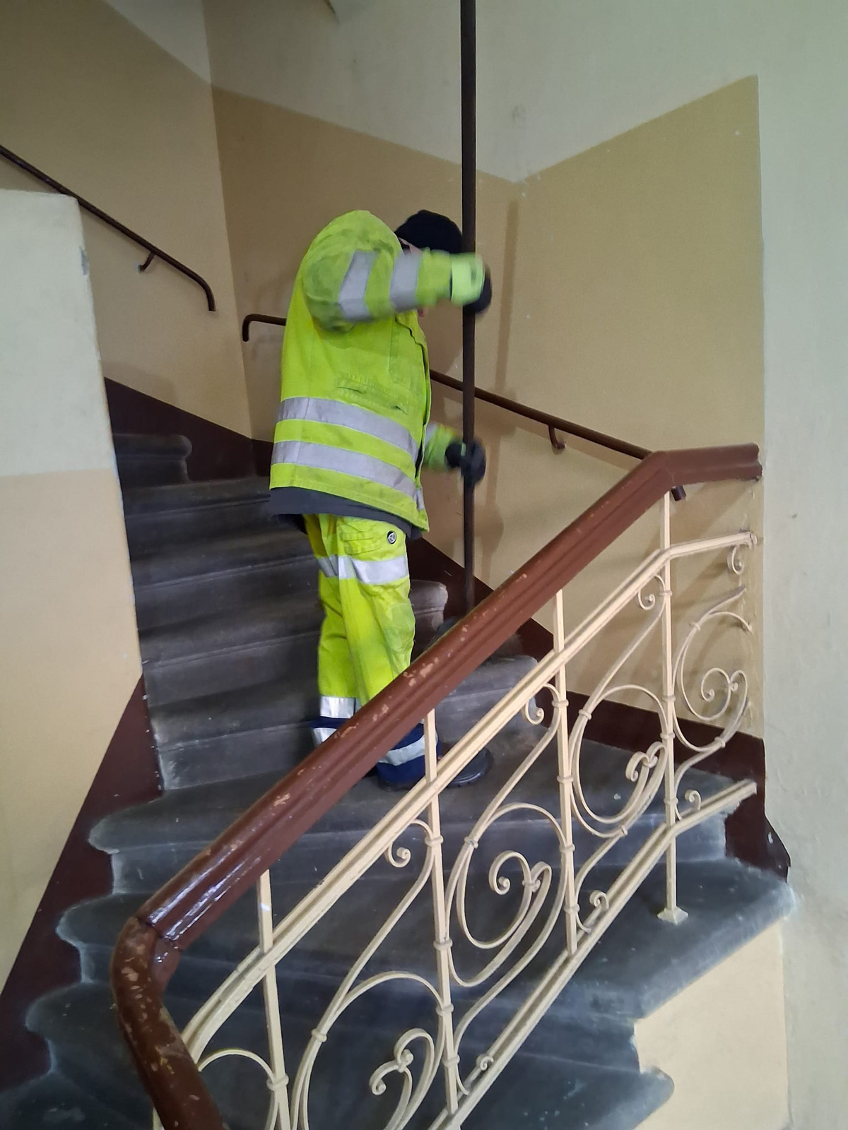 Sprzątanie klatki schodowej w budynku wielorodzinnym, pracownik porządkowy zamiata schody.