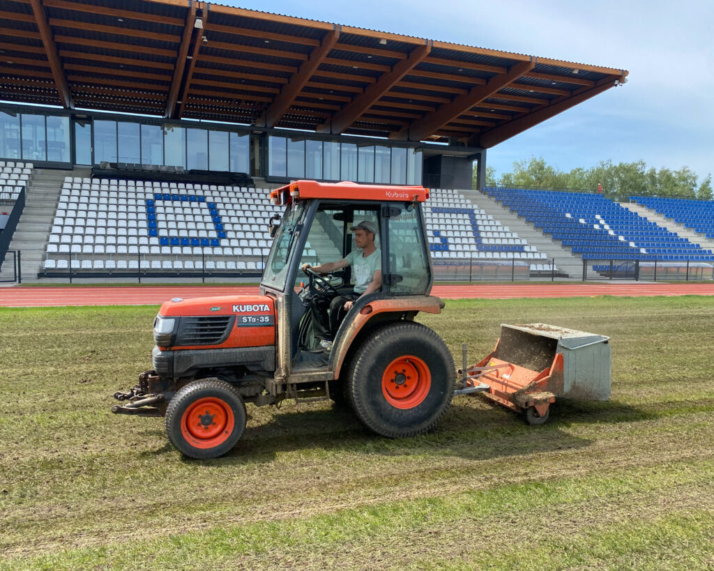 Oczyszczanie i zbieranie filcu z murawy stadionu za pomocą traktora komunalnego.
