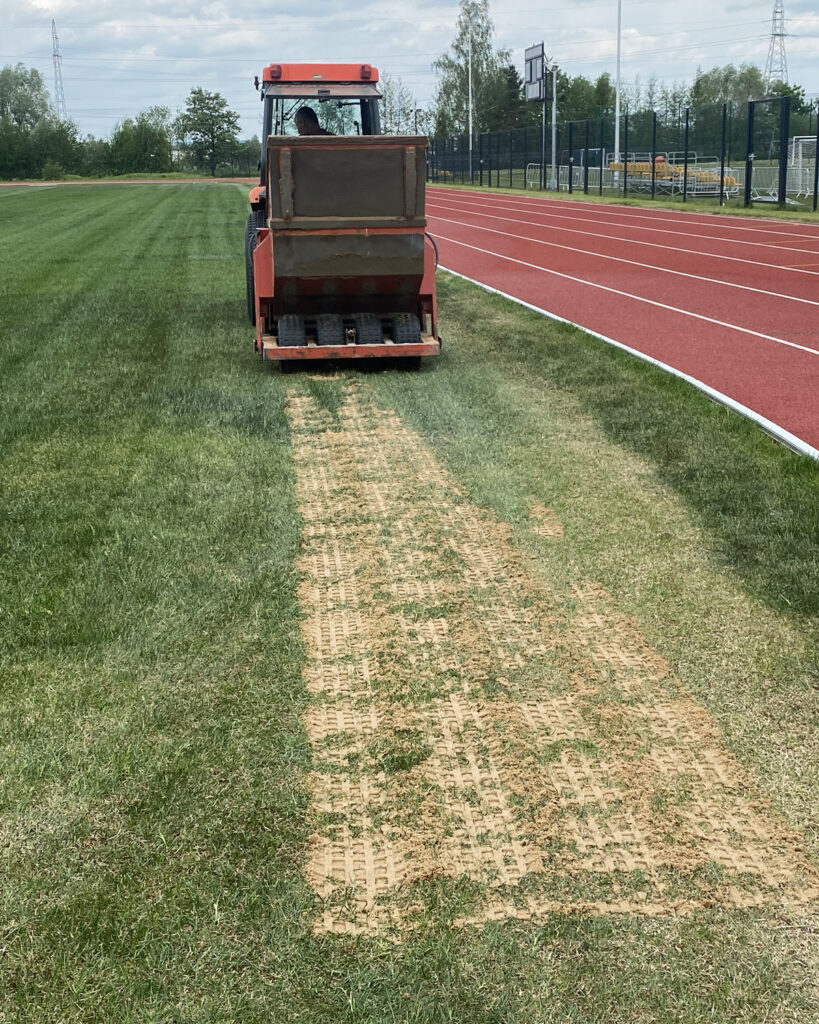 Piaskowanie i wyrównywanie murawy boiska sportowego przy użyciu specjalistycznej piaskarki.
