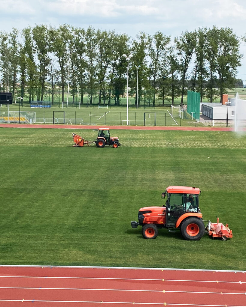 Zabiegi regeneracyjne murawy na stadionie sportowym wykonywane ciągnikami z profesjonalnym sprzętem do pielęgnacji trawy.